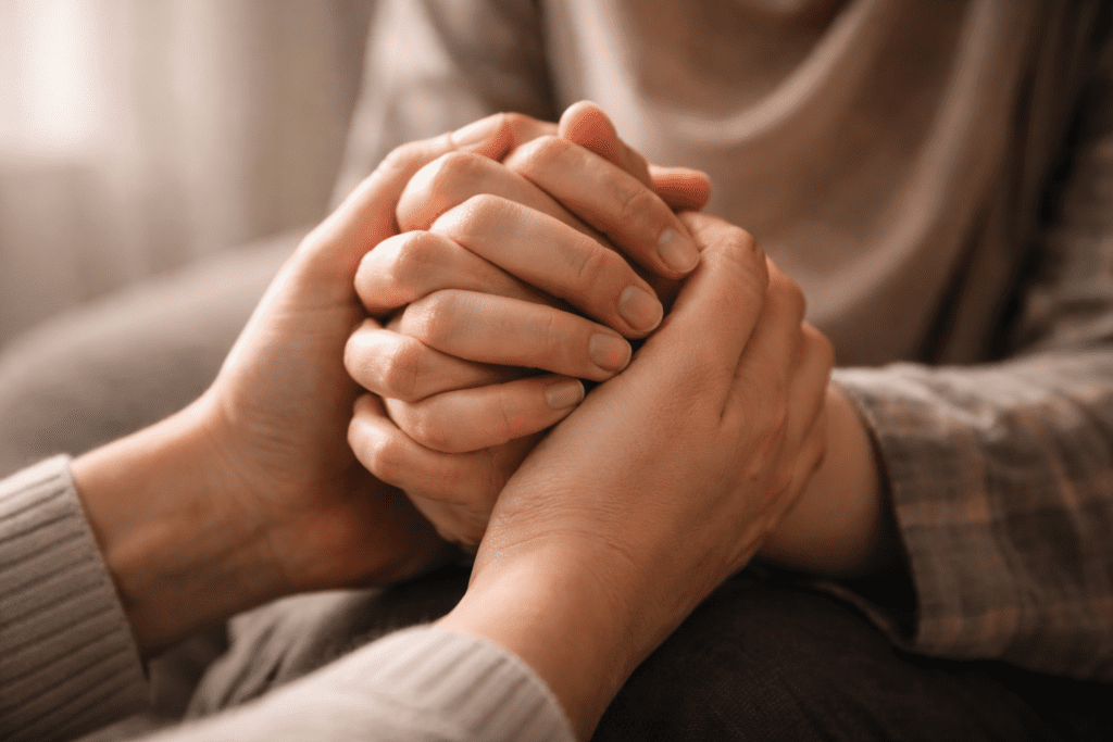Close-up dua pasang tangan, satu berdoa dan satu mendukung, simbol solidaritas dalam doa untuk orang yang mengalami trauma.